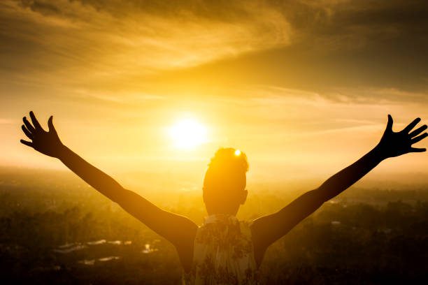 Silhouette of a beautiful black girl raising her arms over the valley as the sun sets